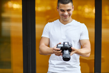 A young man stands outdoors with a camera and adjusts the camera