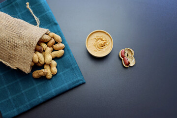 Peanut butter and peanuts in shells on a blue towel on a gray background.