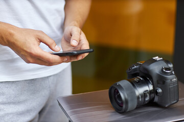 Fototapeta na wymiar A young man stands on the street with a phone in his hands near a table with a camera