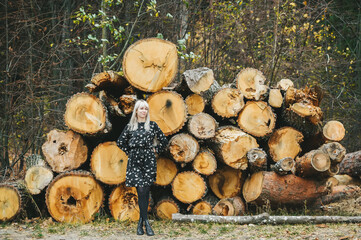 Portrait of cute blonde girl posing against cut tree trunks background in autumn day.