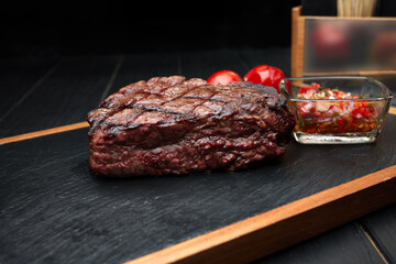Meat steak with vegetables and sauce, on a wooden board with black slate, on a black background