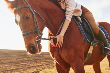 Young woman in protective hat with her horse in agriculture field at sunny daytime