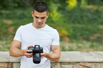 A young man stands outdoors with a camera and adjusts the camera