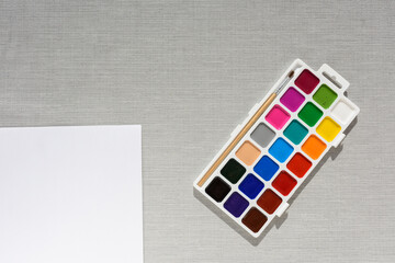 Brush, pallet watercolor paint and empty sheet of paper on grey background. no people. Top view. copy space. Workplace artist. drawing kit. fine art, creativity, painting and artistic tools concept