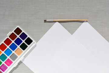 Brush, pallet watercolor paint and empty sheet of paper on grey background. no people. Top view. copy space. Workplace artist. drawing kit. fine art, creativity, painting and artistic tools concept