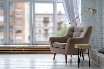  room with a light interior,  beige armchair on  white  floor, a lamp on the background of the window