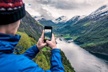 tourist takes photo of Geiranger fjord on smartphone - obrazy, fototapety, plakaty