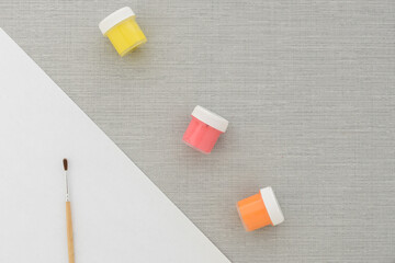 Brush, multi-colored set cans of paint, empty sheet of paper on grey background. no people. Top view. copy space. Workplace artist. drawing kit. fine art, creativity, painting, artistic tools concept