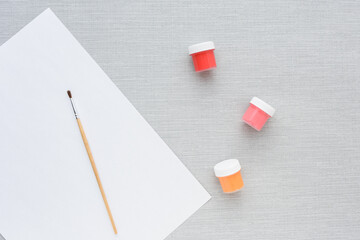 Brush, multi-colored set cans of paint, empty sheet of paper on grey background. no people. Top view. copy space. Workplace artist. drawing kit. fine art, creativity, painting, artistic tools concept