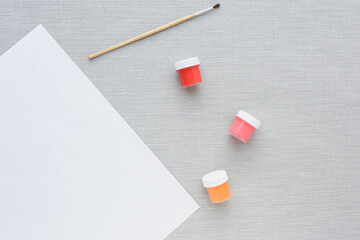 Brush, multi-colored set cans of paint, empty sheet of paper on grey background. no people. Top view. copy space. Workplace artist. drawing kit. fine art, creativity, painting, artistic tools concept