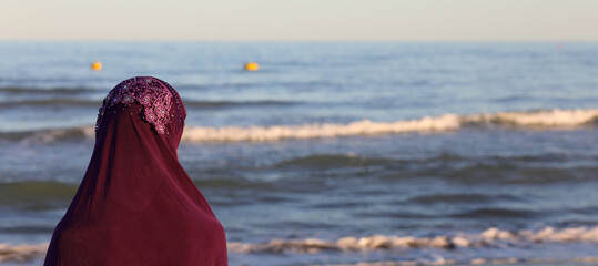 arab girl with veil on her head by the sea waiting for the ship