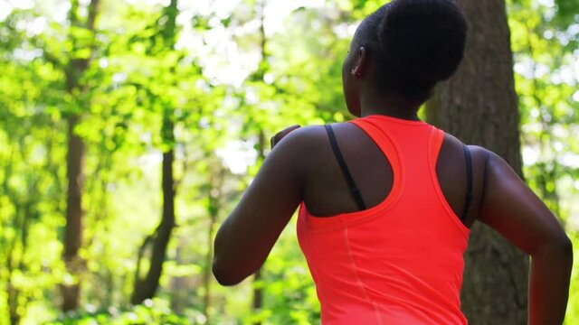 fitness, sport and healthy lifestyle concept - young african american woman running in forest