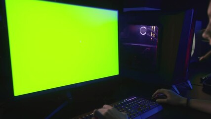 Back view of e cyber sport gamer play game with green screen monitor and powerful personal computer on the table at home