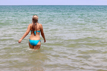 Beach vacation in summer, swimming concept. Blonde woman in blue bikini enjoying the water in a sea