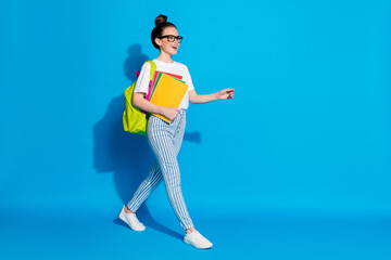 Full size profile side photo of positive college student girl hold books go walk copyspace lesson...