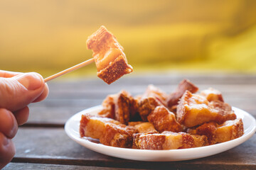 Hand holding a piece of fried pork rinds called “Torreznos” with a toothpick on a dark wooden table. Typicall spanish snacks to eat in a bar. Photo with selective focus. 
