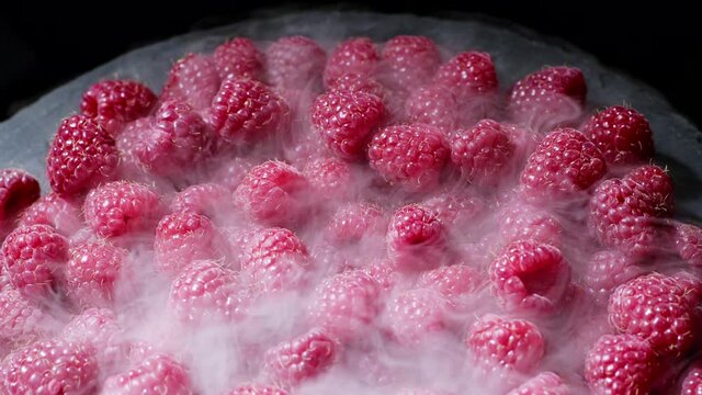 Ripe chilled red raspberries with dry ice steam isolated on dark background. Dieting, vitamins, antioxidants concept. View of delicious dessert.
