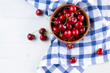 Fresh cherries in a clay bowl on the white table and a kitchen counter in a blue cage. Top view