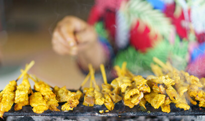 satay or sate, Southeast Asian favorite street food, seasoned, skewered and grilled pork or chicken on charcoal stove, served with peanut sauce