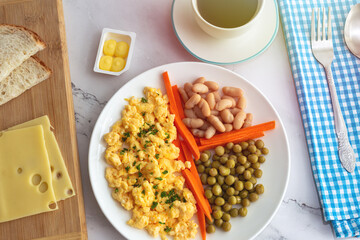 Scrambled eggs, green peas, beans, carrot sticks, bread, cheese with a cup of coffee for breakfast