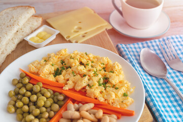 Scrambled eggs, green peas, beans, carrot sticks, bread, cheese with a cup of coffee for breakfast