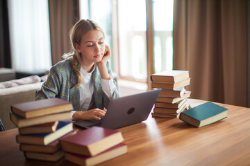 Young cute teen schoolgirl student sitting with books and working at laptop. Back to school. Exam preparation