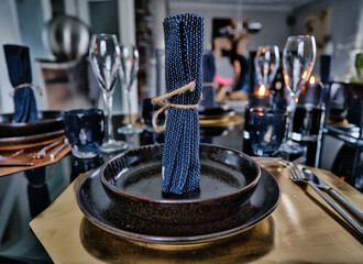 Edel gedeckter Tisch mit schwarzem Geschirr, Champagner Gläser und einer blauen Stoffserviette,...
