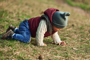 Little boy in warm clothes lying down on ground of field on grass