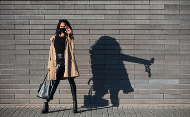 Showing stop gesture by hand. In protective mask. Beautiful brunette with curly hair and in black clothes outdoors near wall