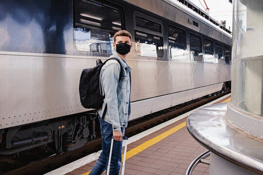Young man wearing protective face mask standing on the railway station near the train.