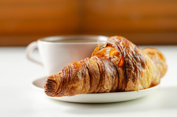 Delicious croissant on a ceramic saucer with coffee in a cup