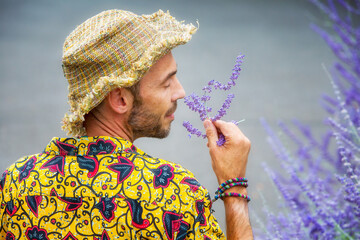 handsome man with straw hat outdoors smelling at purple flowers