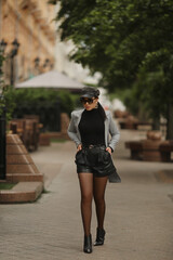 Autumn portrait of the model girl in sunglasses, leather shorts and trendy trench coat walking on the city street