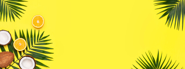 Summer tropical composition. Green tropical leaves of palm trees, coconut, orange on bright yellow background. Flat lay, top view, copy space. Creative background food, fruit