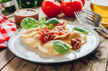 Italian ravioli with meat tomato sauce and basil leaves with on a white dishes on an old rustic background.