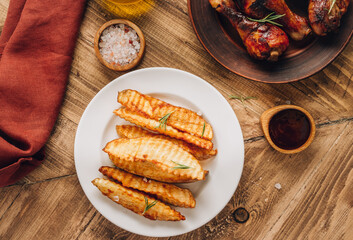 Baked potato fries with sea salt and rosemary and chicken legs on a rustic wooden background. Top view with place for text