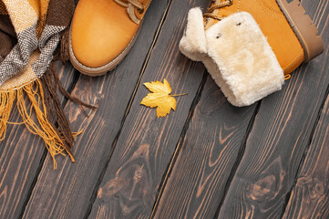 Autumn Fashion Concept. Brown Orange leather women boots with fur, checkered warm plaid, golden autumn leaf on brown wooden background top view. Fashionable women's footwear. Cozy fall composition