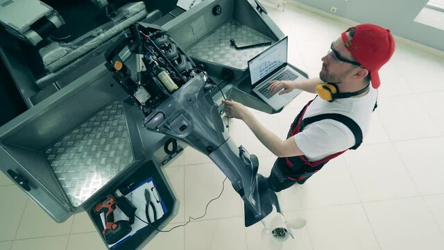 Repairman with a laptop is fixing speedboat's motor