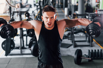 Liting dumbbells. Young sportive strong man in black wear have workout day in gym