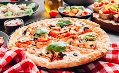 Sliced italian pizza with salami, mozzarella, mushroom, tomatoes, black olives and basil leaves on black background. Italian traditional food. Popular street food concept. Selective focus. Back light