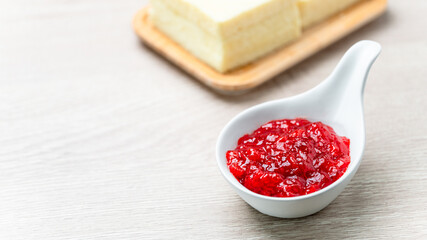 Strawberry Jam in white ceramic cup placed on wooden table with blurred bread background. Food close up