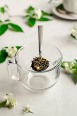 Dry green tea in glass mug, fresh jasmine flowers and leaves on white background