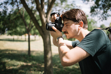 Side view of man with camera taking photos. Close-up view of photographer shooting in nature using professional camera.