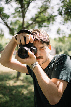 Portrait of man holding camera and taking photos. Male photographer looking through camera viewfinder while taking pictures outdoor.