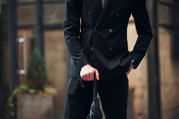 Close up view. Holding umbrella. Elegant young man in formal classy clothes outdoors in the city