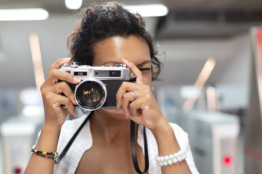 Close-up of a woman with exotic features taking a picture with an analog film camera. Selective focus. Concept of travel and tourism.