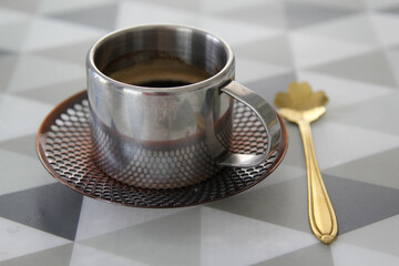 A stainless steel coffee cup with black coffee on the table.