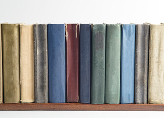 A row of old, faded, multicolored, yellowed books on a light background. Minimal style, copy space, side view