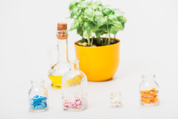 selective focus of green plant in flowerpot near pills in glass bottles and essential oil on white background, naturopathy concept