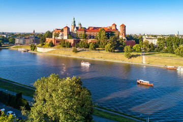 Fototapeta premium Royal Wawel Cathedral and castle in Krakow, Poland. Aerial view in sunset light. Vistula River, tourist boats, riverbanks with parks, trees. promenade and walking people
